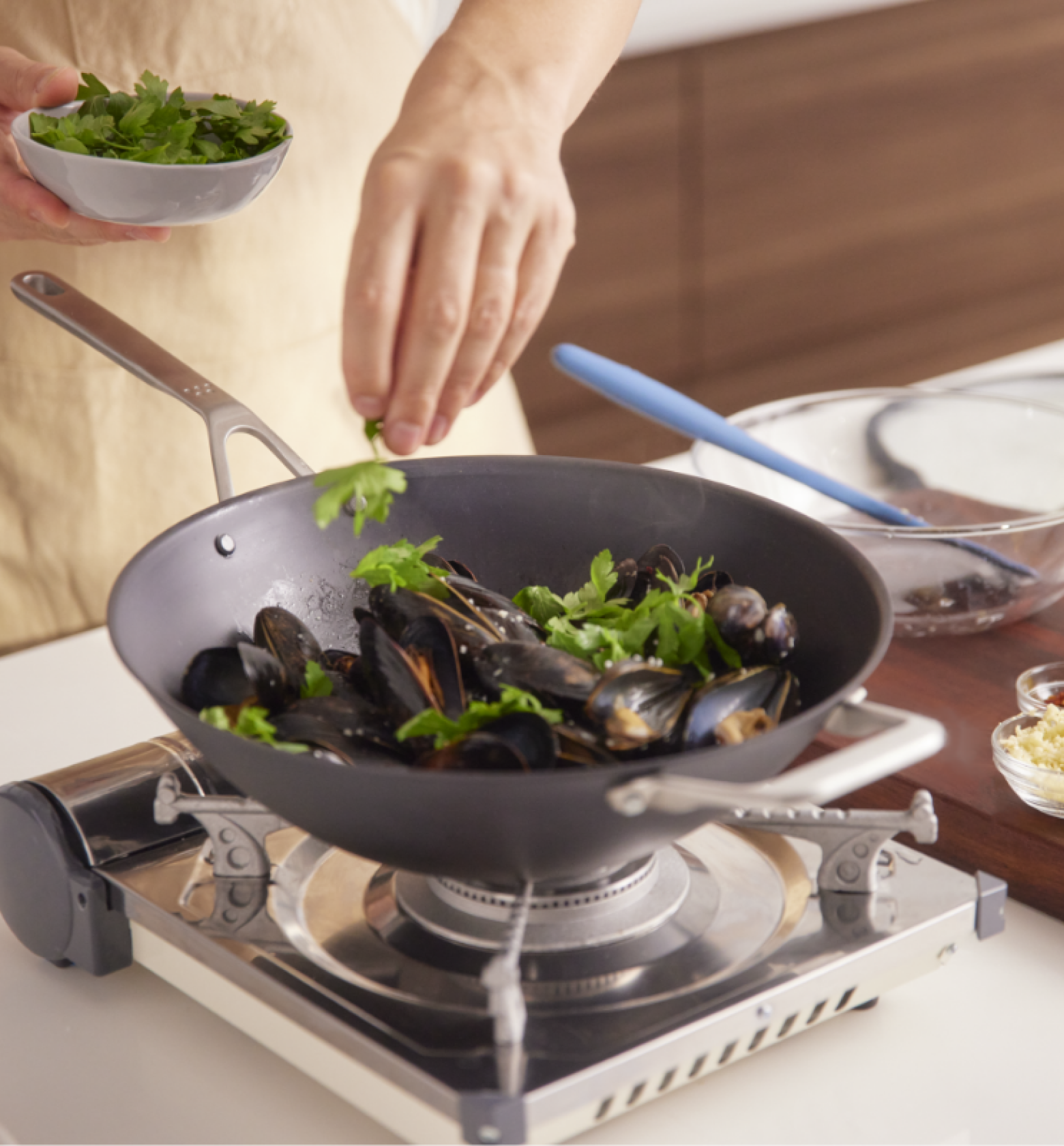 Chef adding fresh parsley to steamed mussels in a wok on a portable gas burner